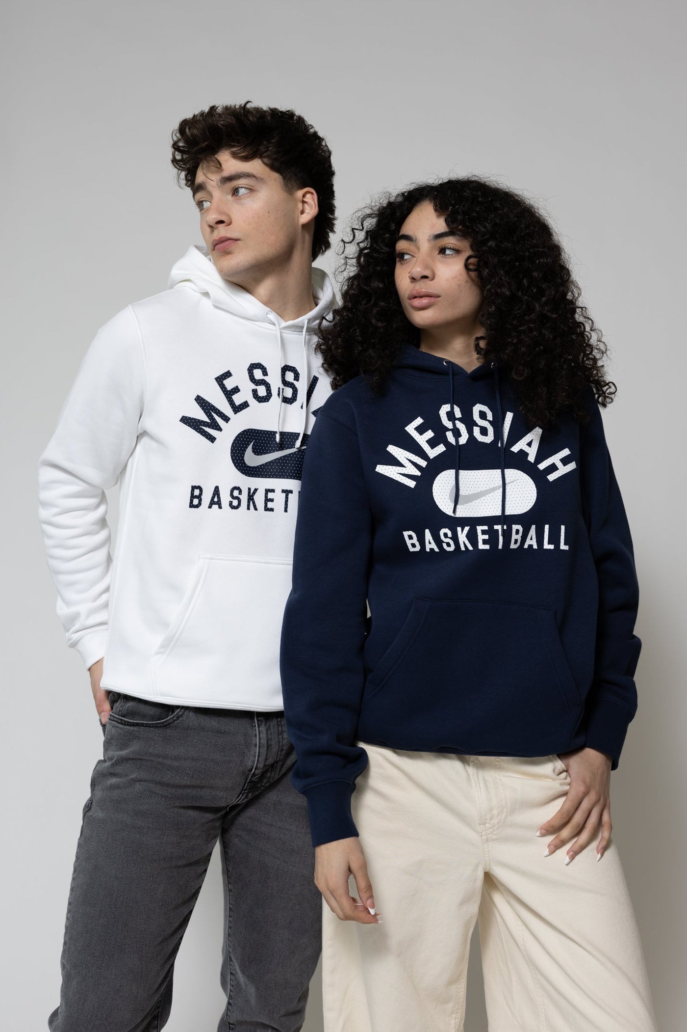 Two people wearing 'Messiah Basketball' hoodies on a plain background