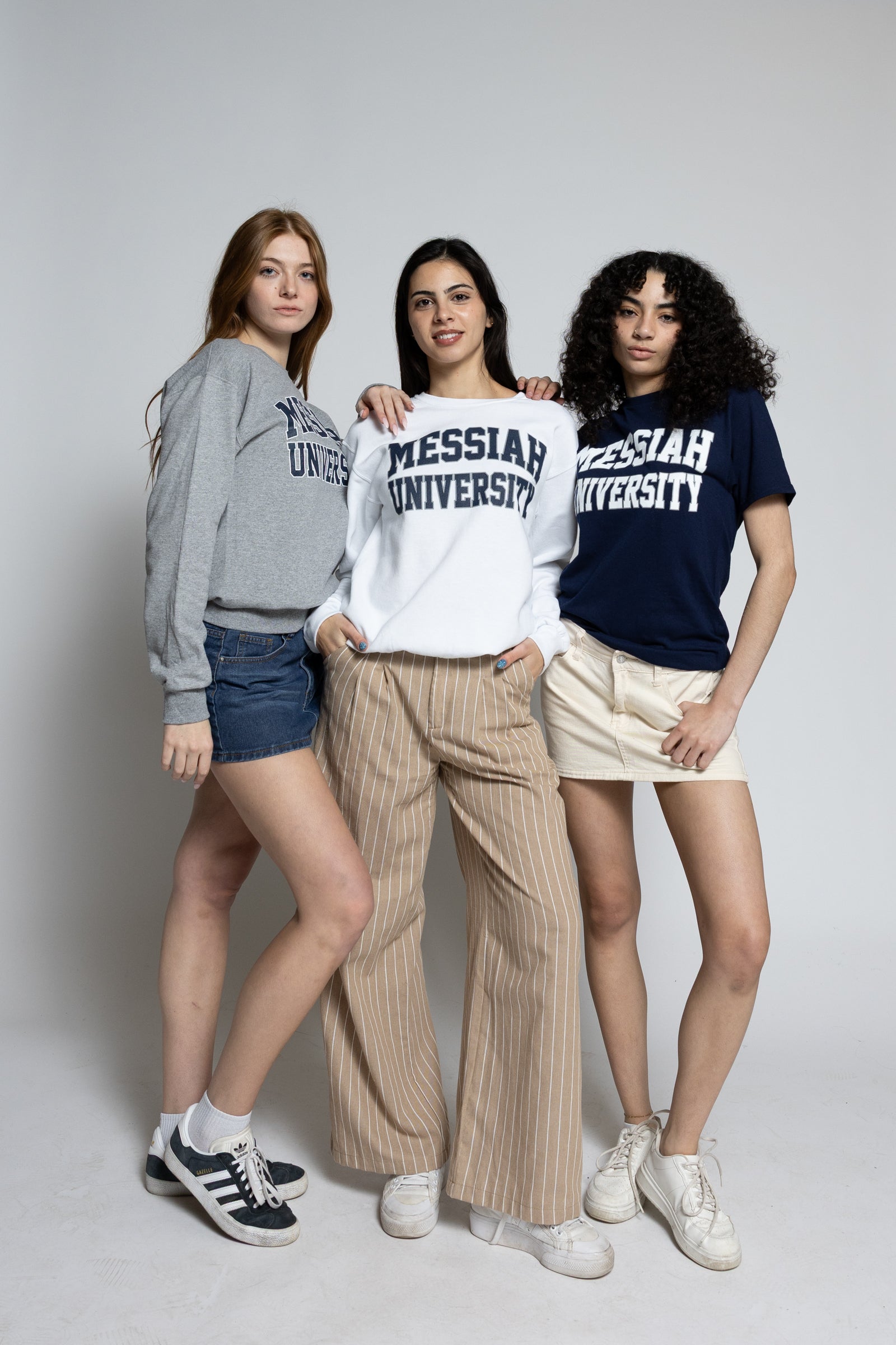 Three women wearing Messiah University clothing on a plain background