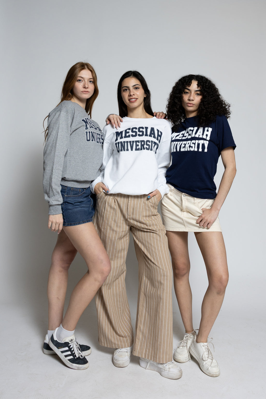 Three women wearing Messiah University clothing on a plain background